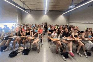 Students sitting in a classroom smiling at the camera and holding up signs that say "sí."